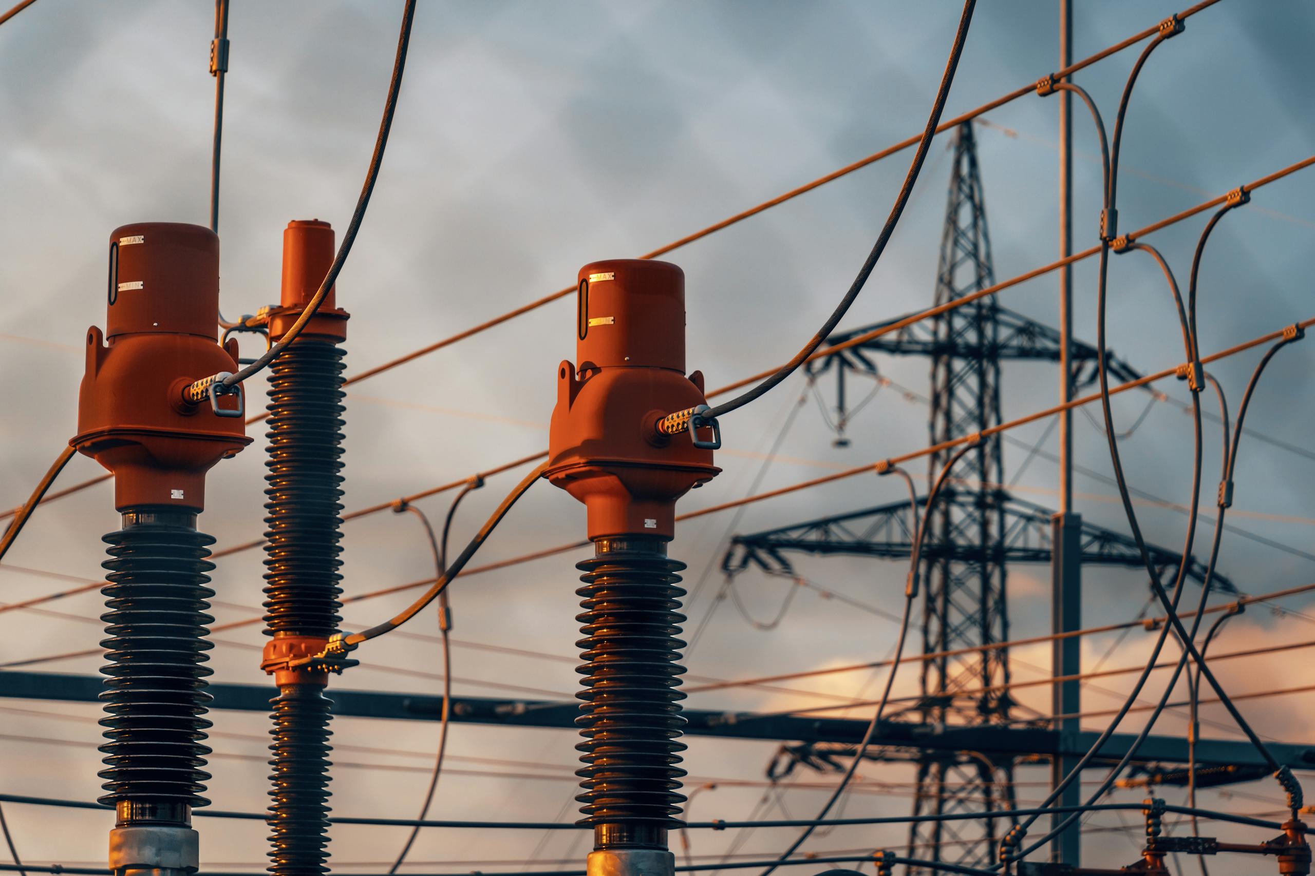 A towering steel pylon supporting multiple electric power lines in an industrial landscape.
