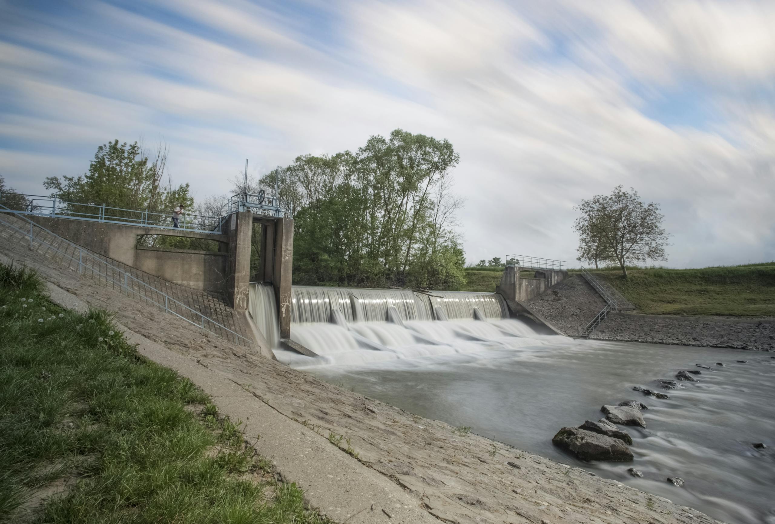 Long exposure of water flow over a dam with blurred motion and serene surroundings.